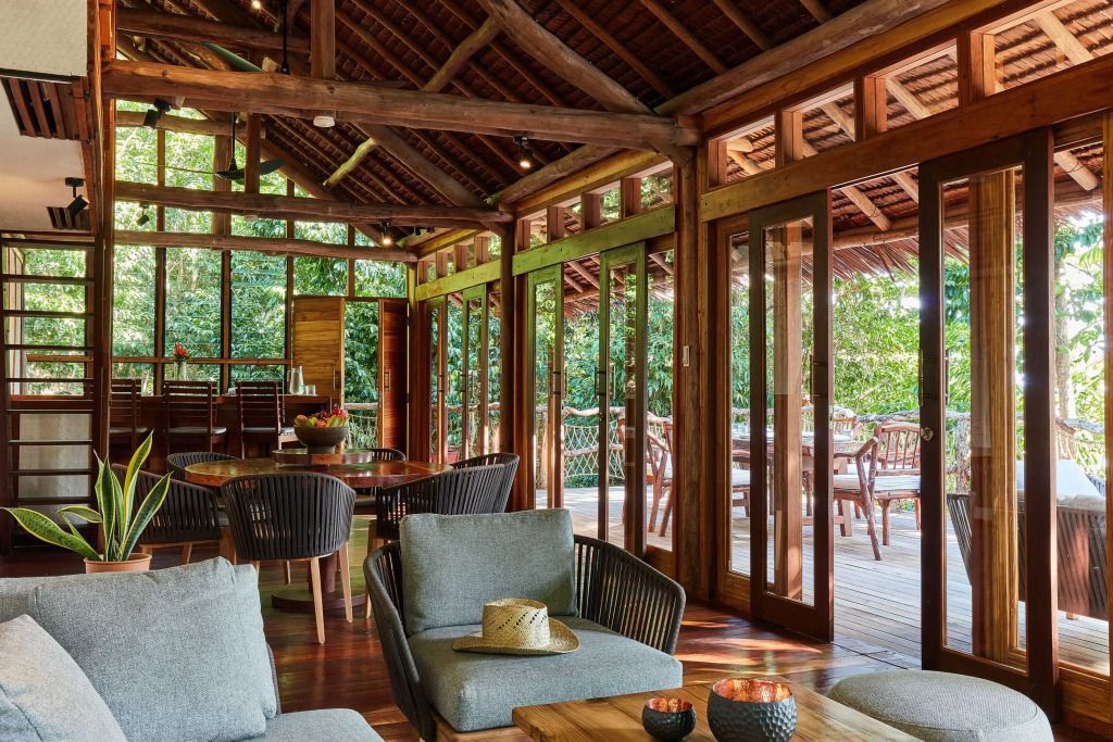 Helles Wohnzimmer mit großzügigen Fenstern und eleganten Rattanmöbeln in tropischer Umgebung.