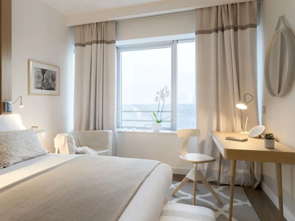 Helles Schlafzimmer mit großem Fenster und Meerblick. Schreibtisch und Dekorationen vorhanden