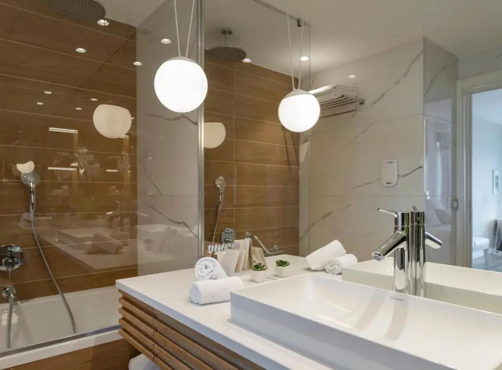 Modernes Badezimmer mit weißem Waschbecken, hängenden Leuchten und eleganter Dusche.