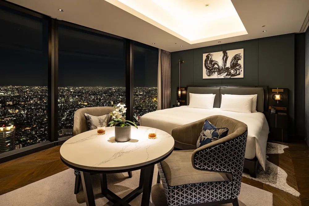 Elegantes Zimmer mit Doppelbett, Kunst an der Wand und Blick auf die beleuchtete Stadt bei Nacht.