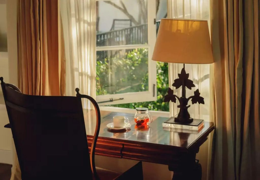 Gemütlicher Schreibtisch am Fenster mit Blick ins Grüne und eleganter Lampe