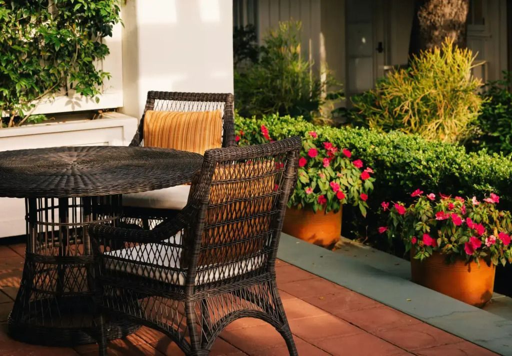 Terrasse mit Rattan-Möbeln umgeben von grünen Pflanzen und Blüten.