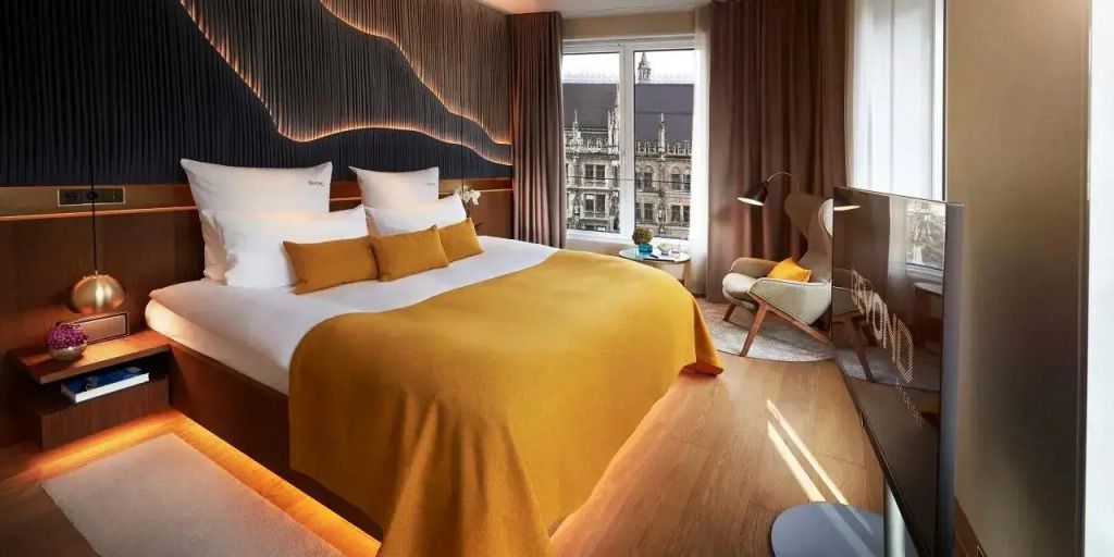 Moderne Hotelzimmer mit Doppelbett und Blick auf historischen Platz durch große Fenster