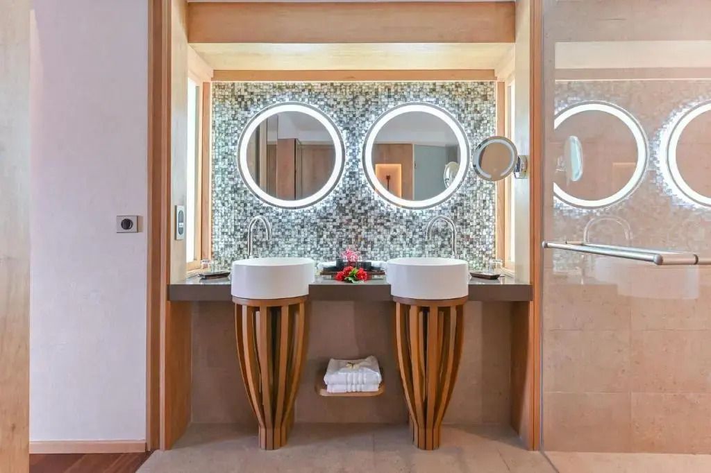 Moderne Doppelwaschbecken im Badezimmer eines Überwasser-Bungalows mit beleuchteten Spiegeln.