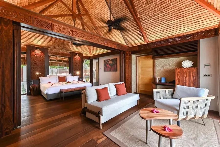 Geräumige Villa mit Holzmöbeln, gemütlicher Sitzecke und Blick auf ein luxuriöses Bett.