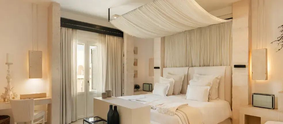 Helles Doppelzimmer mit stilvollem, weißem Baldachin am Doppelbett und Balkonzugang.