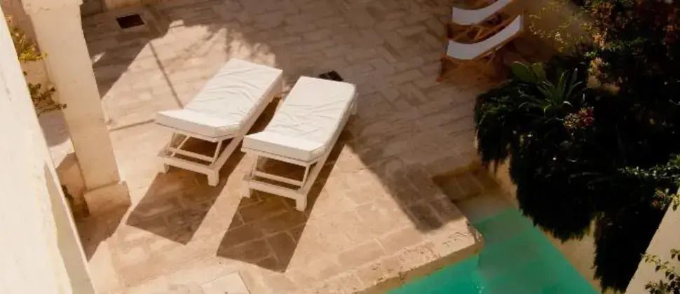 Zwei Sonnenliegen auf einer Terrasse neben einem klaren Pool in mediterraner Umgebung.