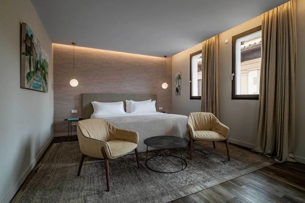 Elegantes Schlafzimmer mit Doppelbett, zwei Sesseln und Wandlampen in der Junior-Suite