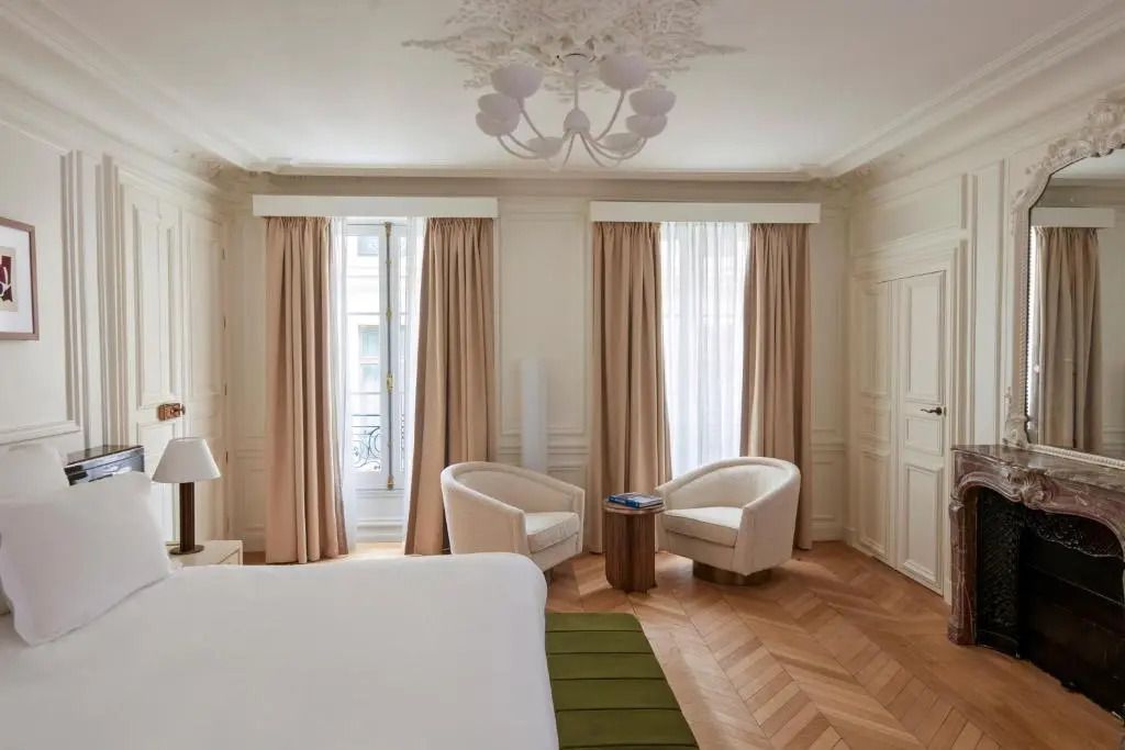 Helle Junior-Suite mit zwei Sesseln und großen Fenstern mit Beige-Vorhängen