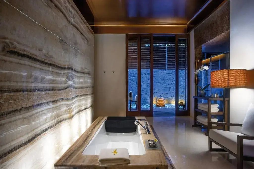 Luxuriöses Badezimmer mit versenkter Steinwanne und Natursteinwand im Bvlgari Resort Bali