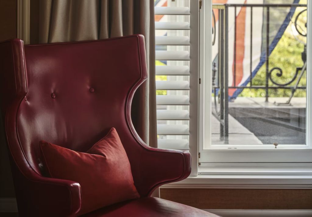 Detailaufnahme eines eleganten roten Sessels neben einem Fenster mit weißen Jalousien