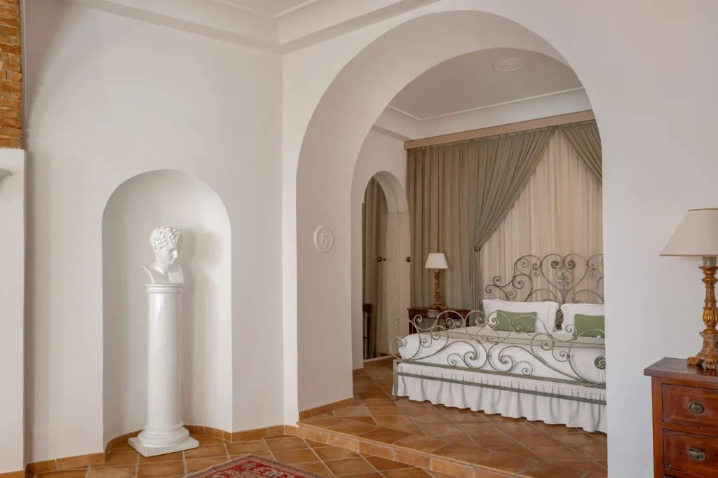 Elegantes Schlafzimmer mit schmiedeeisernem Doppelbett und klassischer Büste in Nische