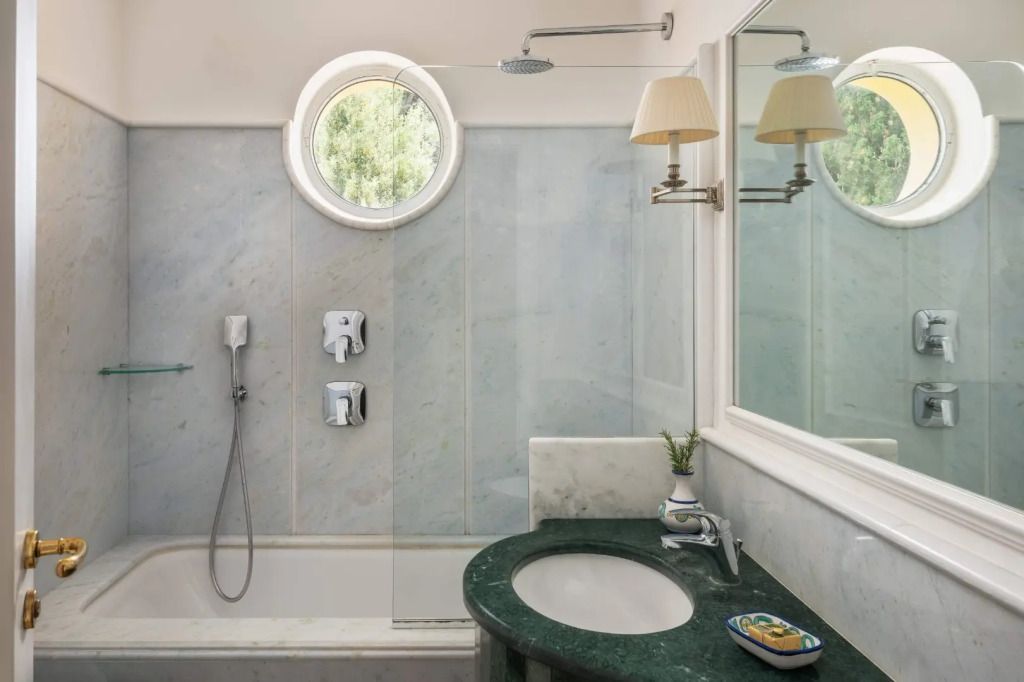 Stilvolles Badezimmer mit Marmorwänden, runder Fensteröffnung und eleganter Beleuchtung
