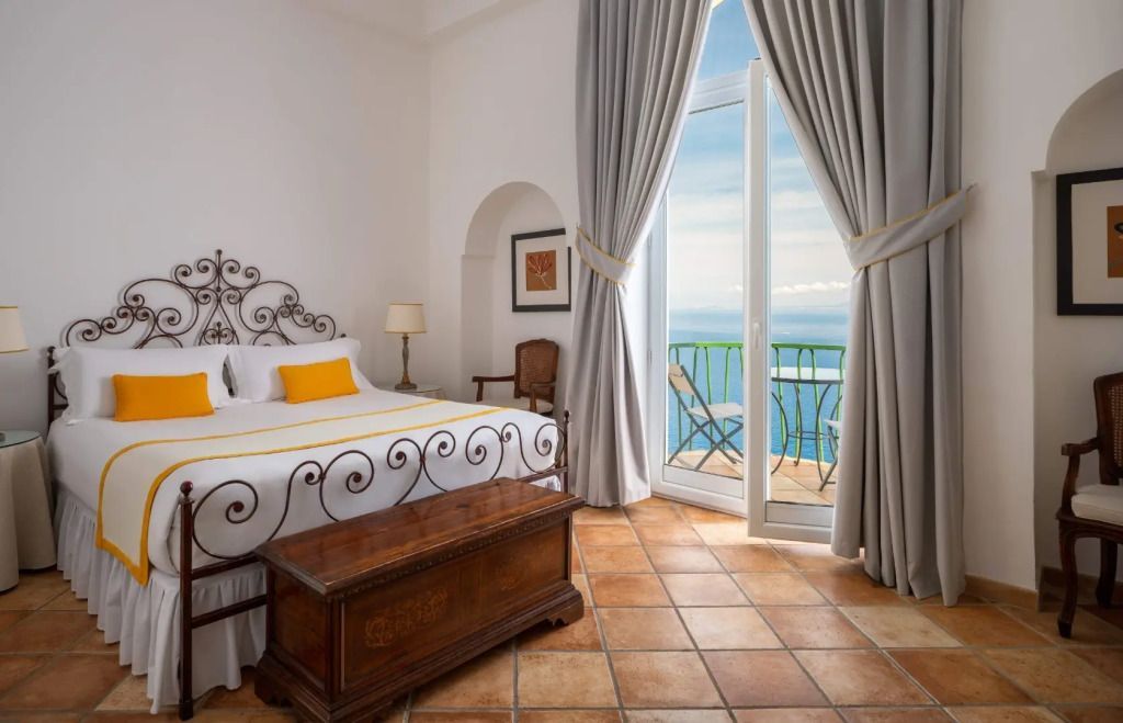 Helles Zimmer mit Doppelbett und Meerblick durch große Fenster.