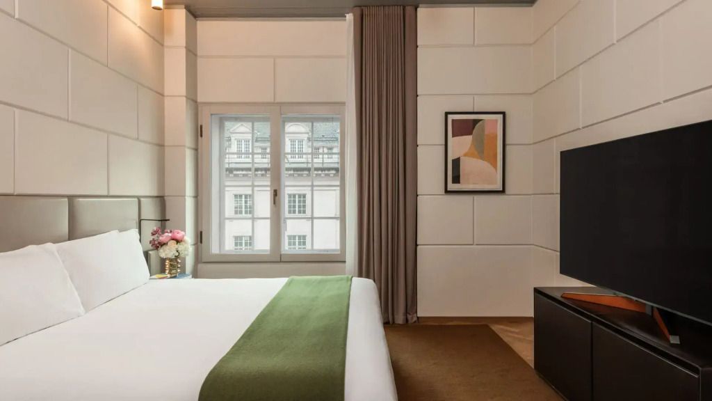 Elegantes Hotelzimmer mit großem Bett, modernem Design und Blick auf Gebäude.