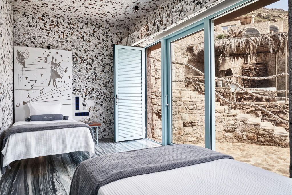 Helles Schlafzimmer mit großen Fenstern und Blick auf eine Steinmauer.