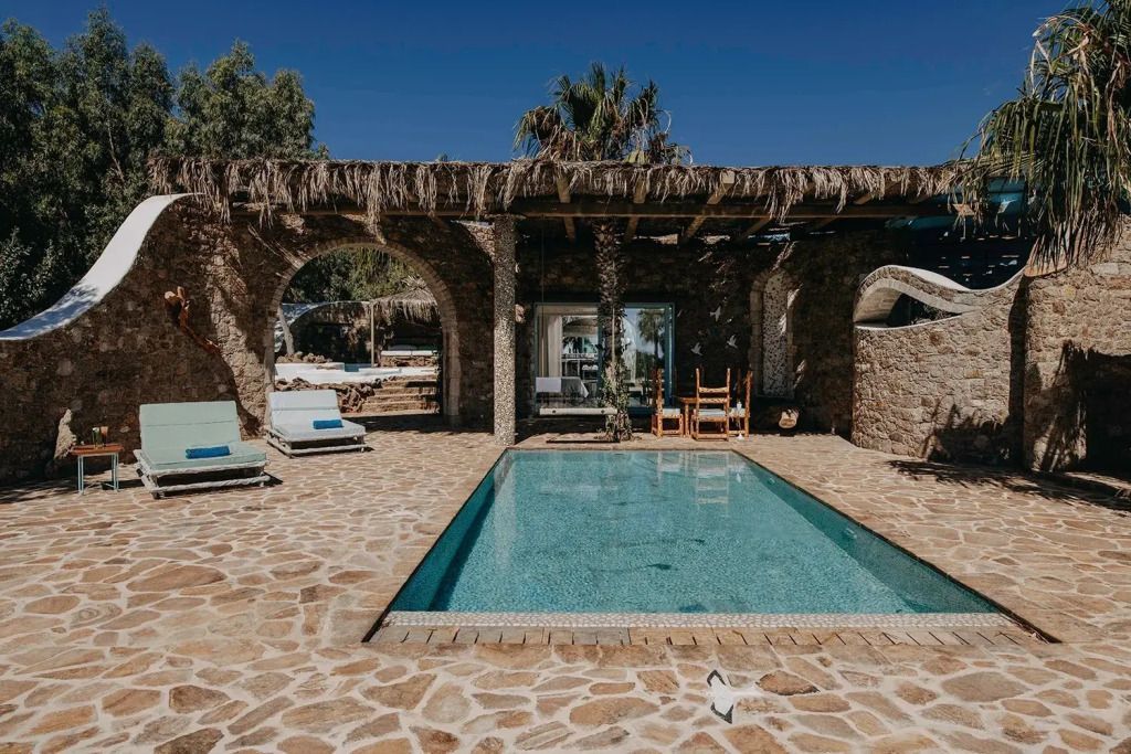 Privater Pool mit Sonnenliegen und Natursteinfassade unter blauem Himmel