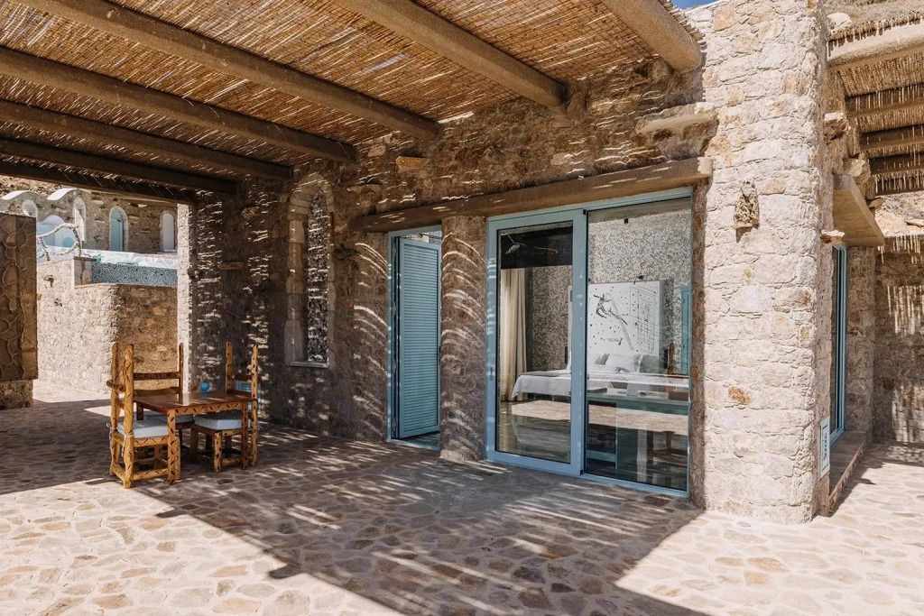 Steinveranda mit Blick auf die Innenräume der Suite. Tisch und Stühle unter Pergola