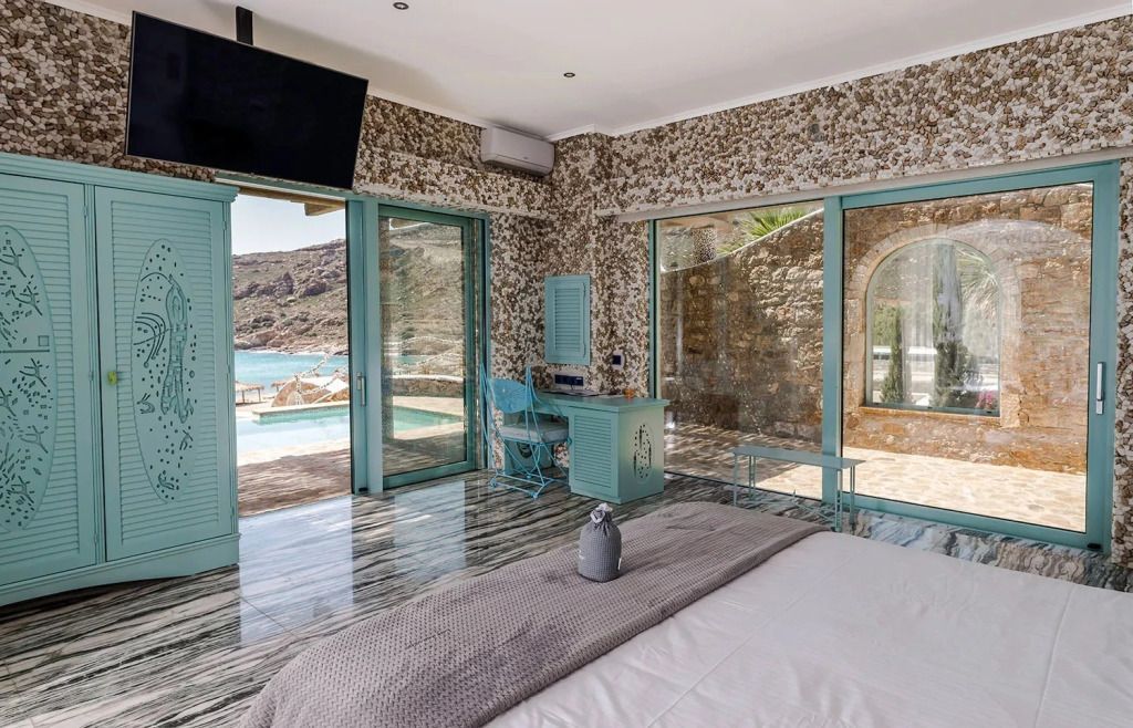 Helles Schlafzimmer mit Blick auf den Pool und das Meer durch große Glastüren.