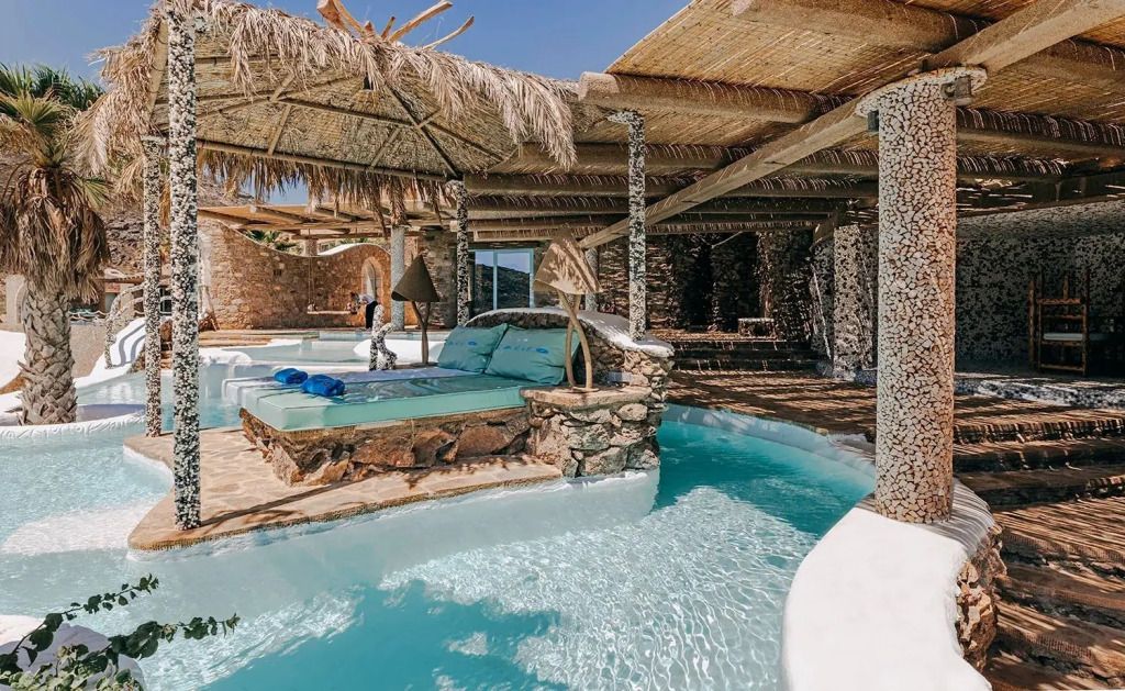 Poolbereich mit Sonnenliegen unter schattenspendenden Palapa-Schirmen aus Stroh.