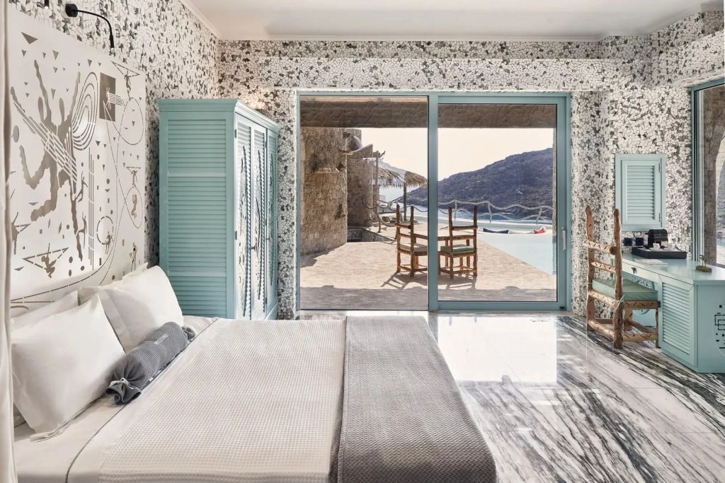 Helles Schlafzimmer mit Doppelbett und Ausblick auf Meerterrasse durch große Fenster.