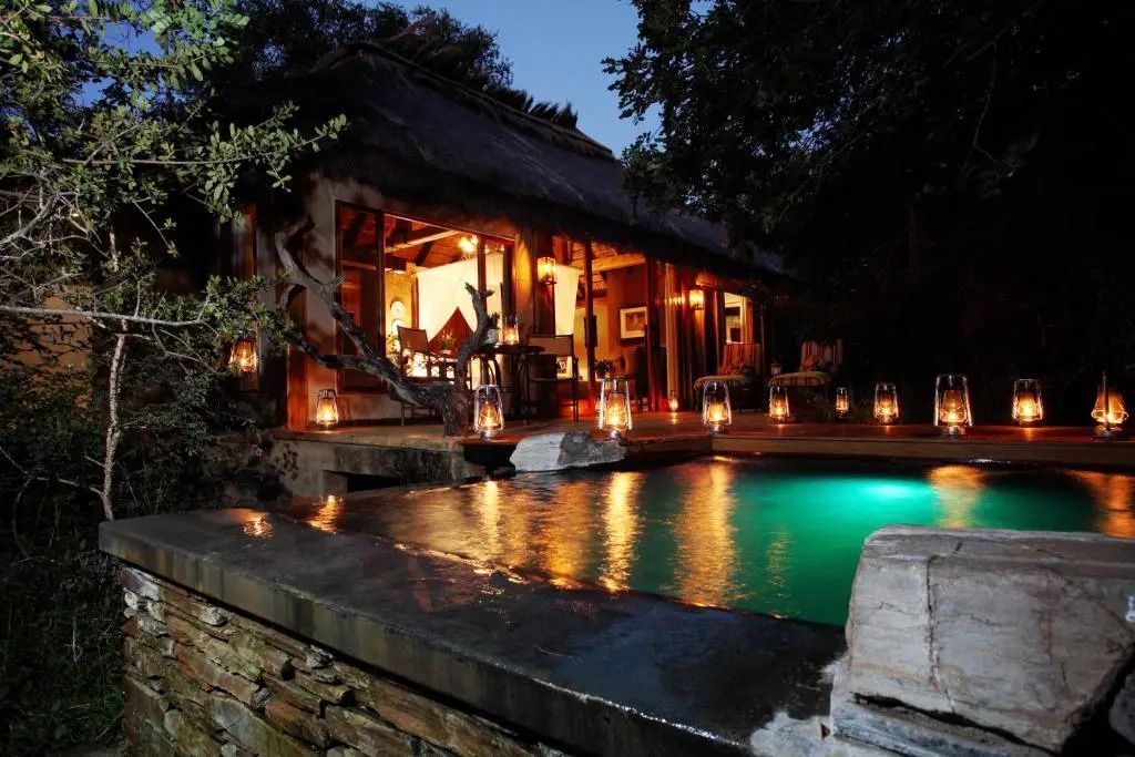 Beleuchteter Pool vor einer Suite am Abend mit umgebenden Laternen