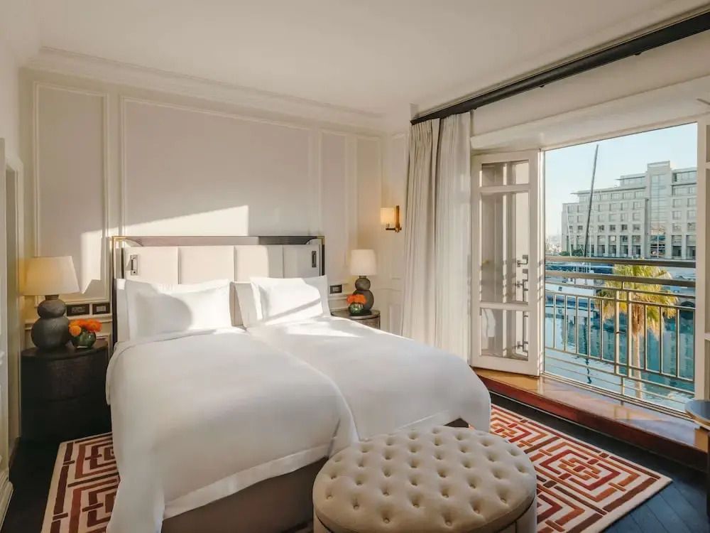 Helles Zimmer mit Doppelbett und Balkon mit Hafenaussicht.