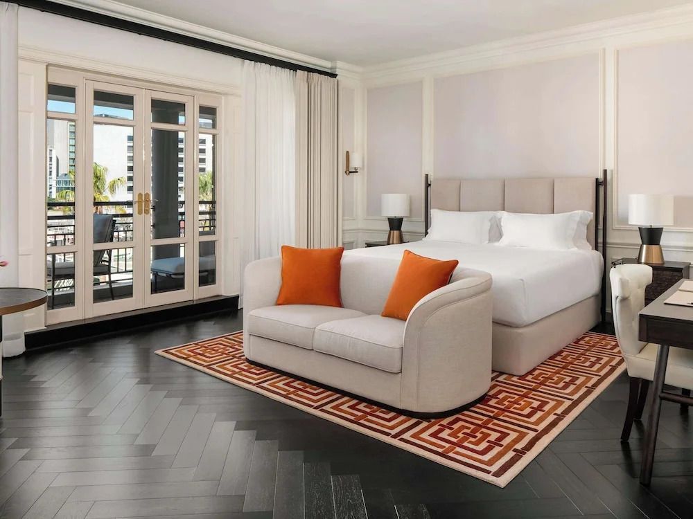 Helles Zimmer mit Kingsize-Bett, Sofa und Balkon mit Blick auf die Stadt.