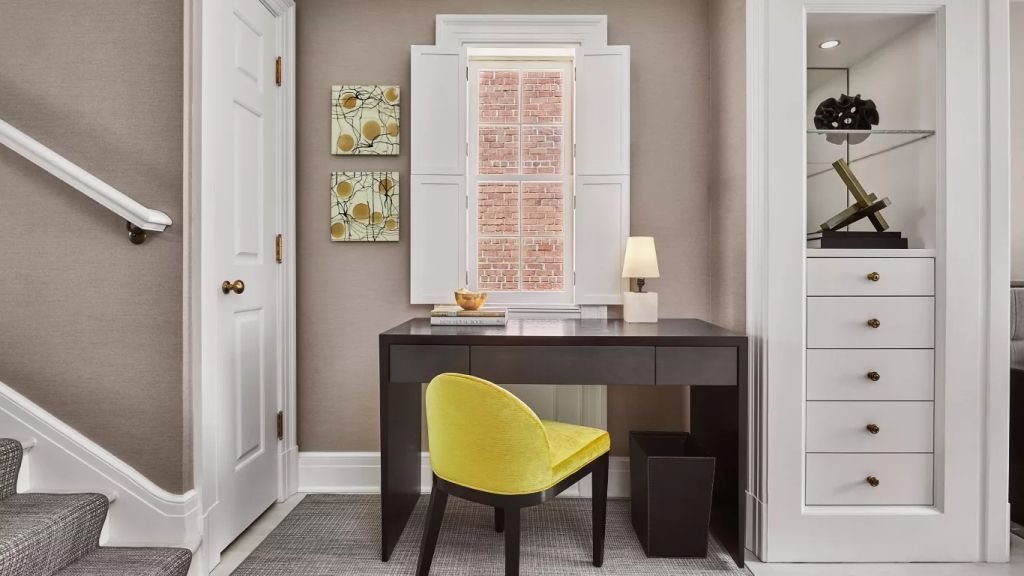 Arbeitsplatz im Hotelzimmer mit Schreibtisch, gelbem Stuhl und Fensterblick.