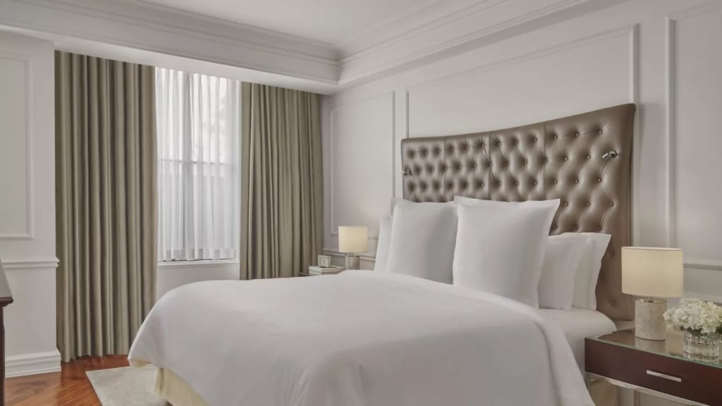 Elegantes Schlafzimmer mit gepolstertem Kopfteil und großen Fenstern in einer Suite.