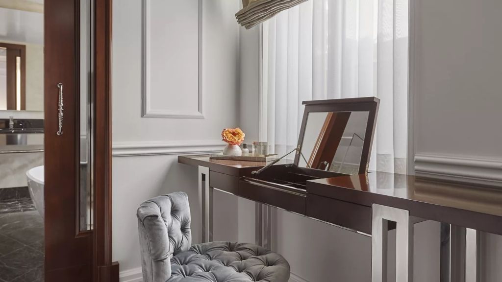 Schicker Schminktisch mit elegantem Stuhl vor einem großen Fenster im Suite-Interieur.