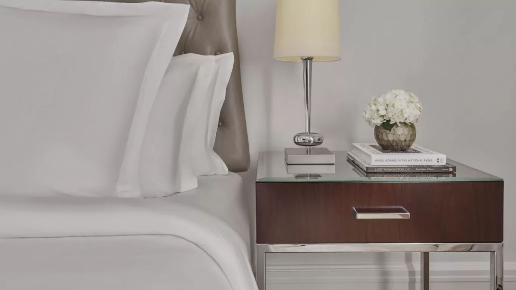 Nachttisch mit Lampe und Blumen neben einem luxuriösen Doppelbett