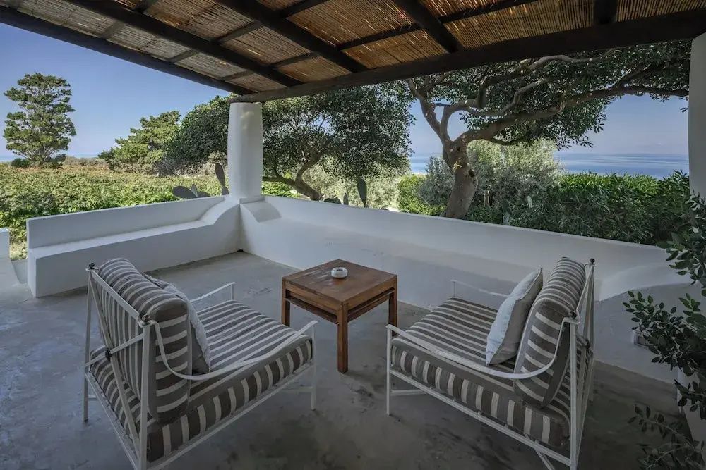 Überdachter Balkon mit gestreiften Stühlen und Blick auf das Meer umgeben von Natur