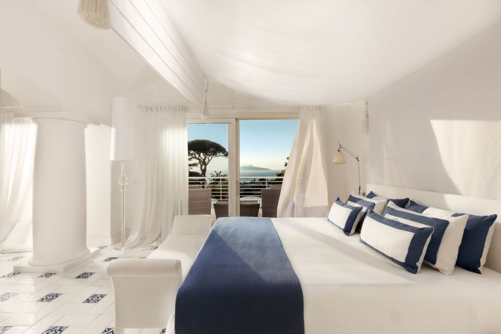 Helle Suite mit Doppelbett, blauen Akzenten und Blick auf Meer und Bäume
