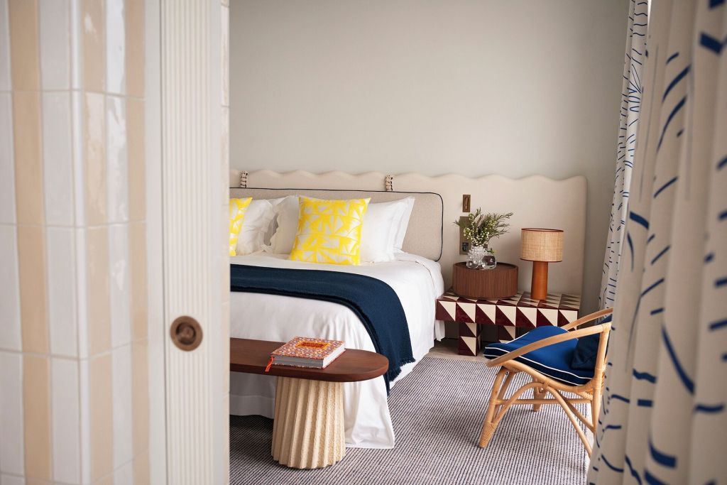 Stilvolles Schlafzimmer mit Doppelbett, bunten Kissen und Holzbank in modernem Design
