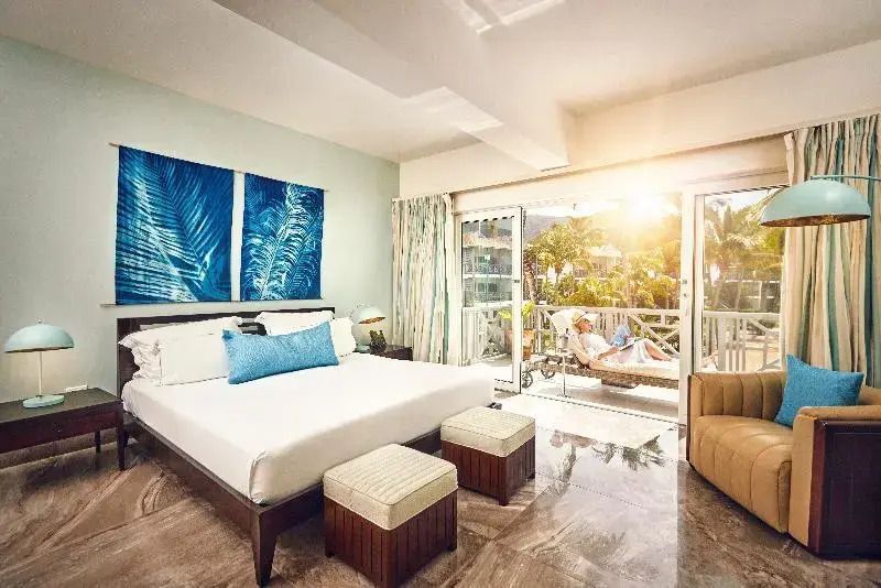 Luxuriöses Hotelzimmer mit großem Bett und Balkon mit Blick auf Palmen.