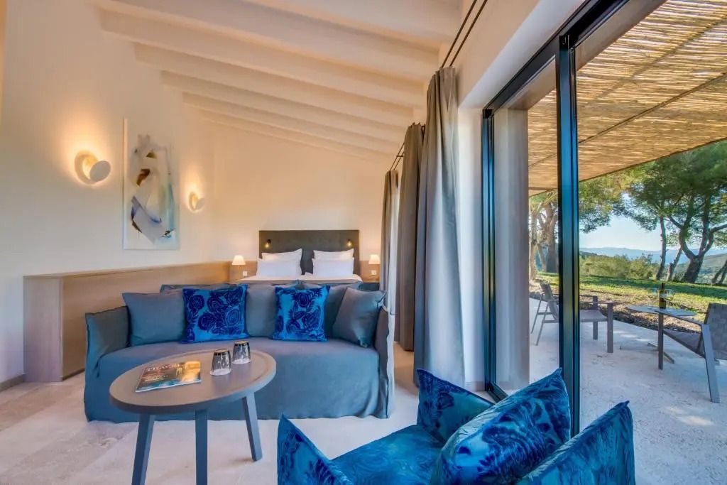 Elegantes Hotelzimmer mit blauer Couch und großem Fenster zur Terrasse