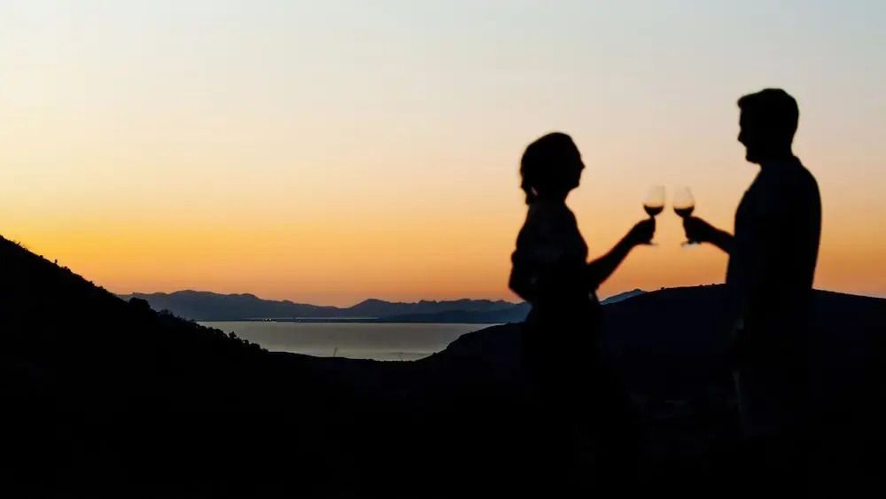 Stimmungsvolle Silhouette mit Wein bei Sonnenuntergang und Blick auf Bucht