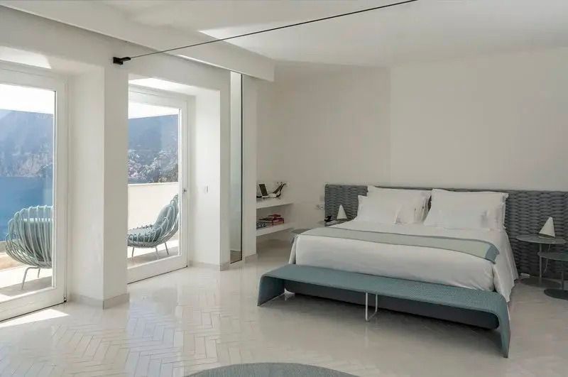 Helles Schlafzimmer mit Doppelbett und Balkon mit Blick auf die Küste.
