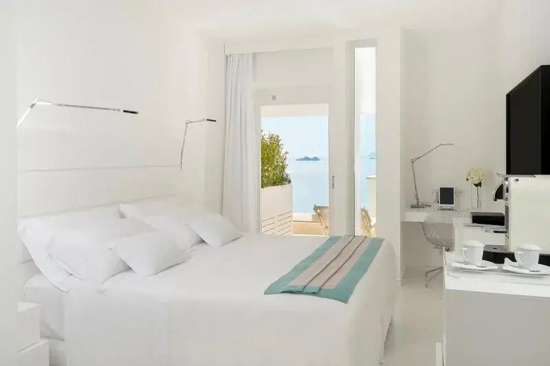 Helles Doppelzimmer mit weißen Möbeln und Meerblick auf Balkon.