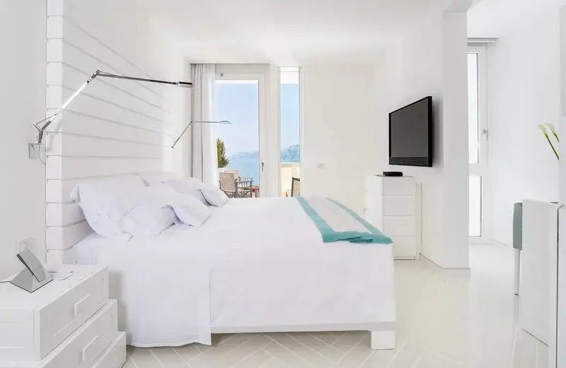 Geräumiges Doppelzimmer mit weißer Einrichtung und großen Fenstern zum Meer.
