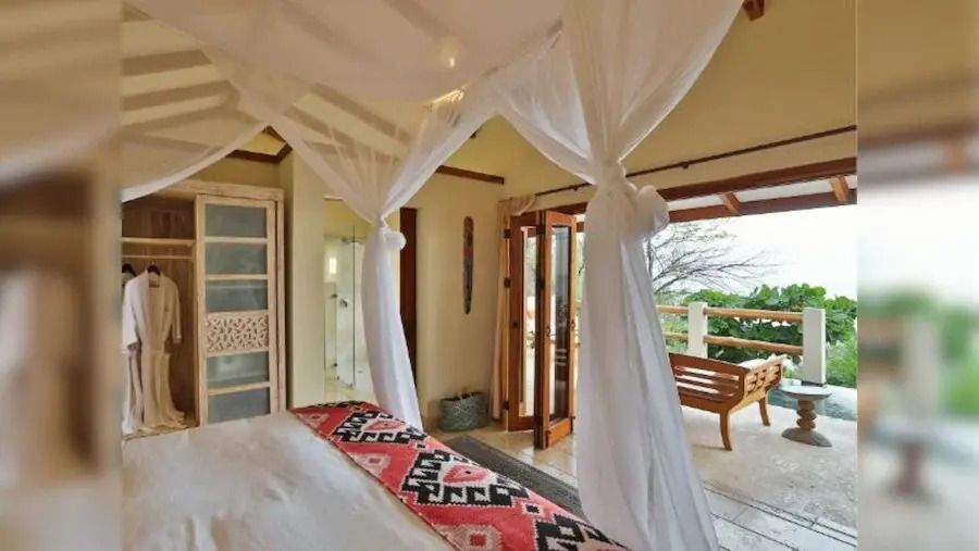 Offenes Schlafzimmer mit Blick auf Terrasse mit Liegestuhl und Meer.