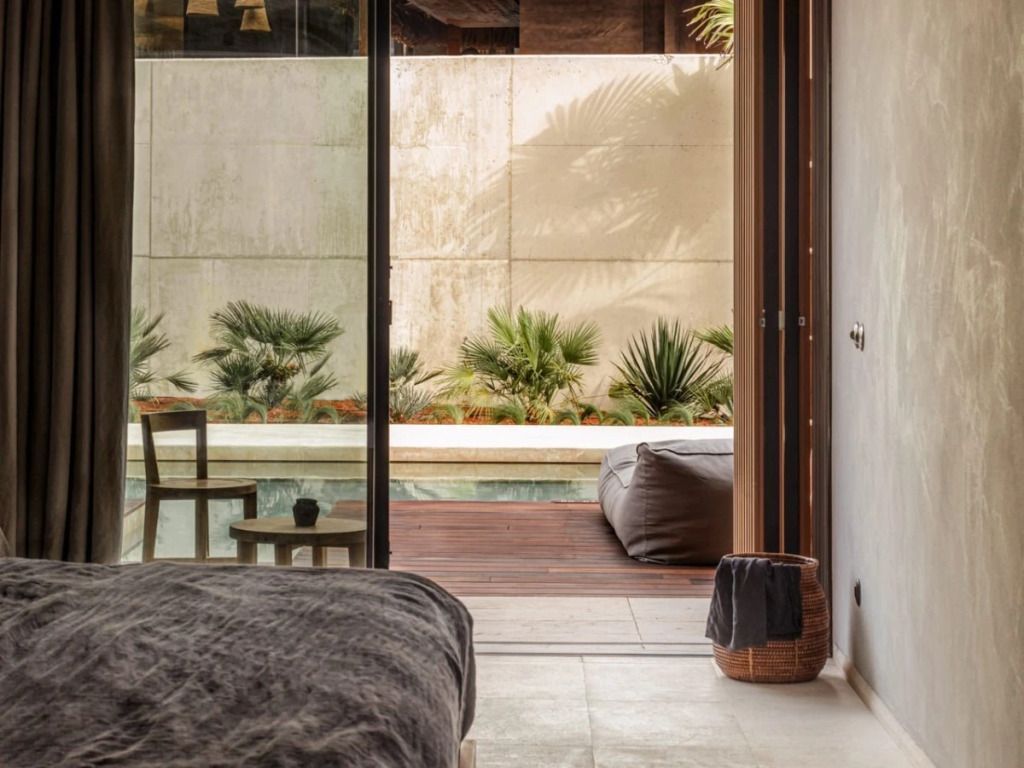 Blick vom Bett auf Poolbereich mit Grünpflanzen und Terrasse