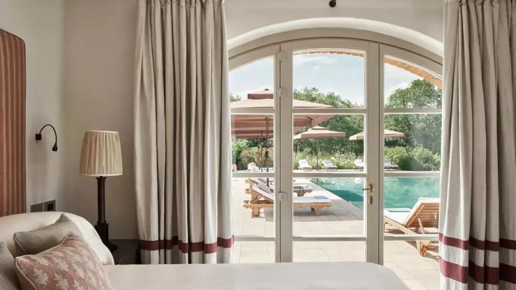 Ausblick vom Schlafzimmer auf den Außenpool mit Liegestühlen und Sonnenschirmen.
