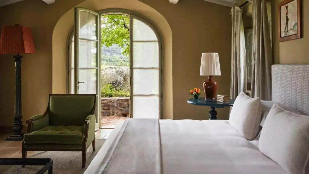 Helles Schlafzimmer mit Bett, Tischlampe und Blick auf Garten durch Glastür.