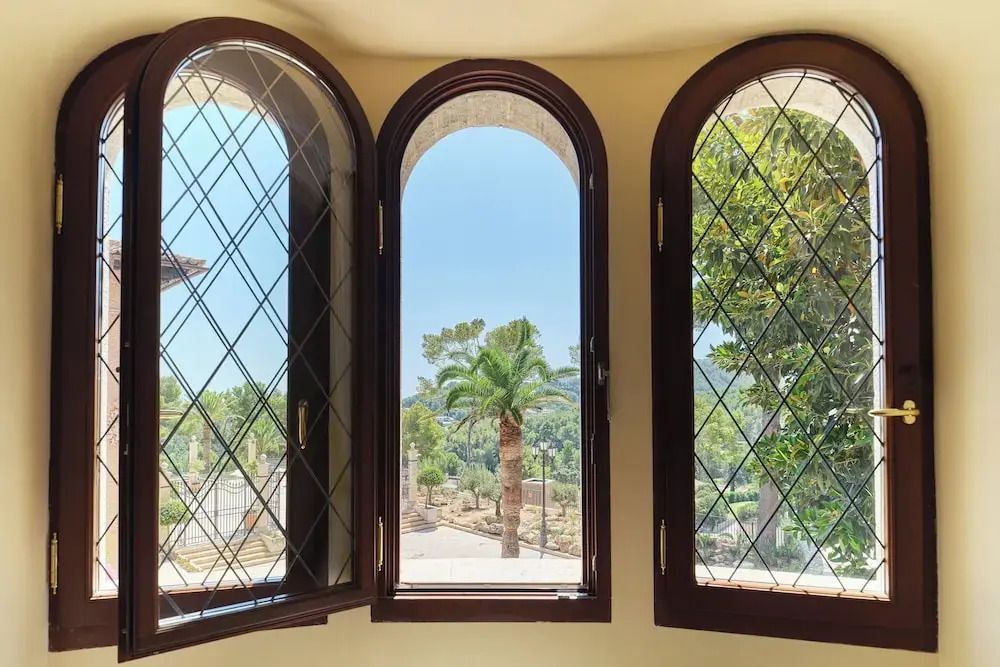 Durch drei dekorative Fenster blickt man auf Palmen und Garten des Hotels