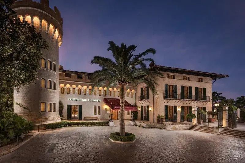 Elegante Steinarchitektur des Castillo Hotel Son Vida bei Abenddämmerung mit Palmen.