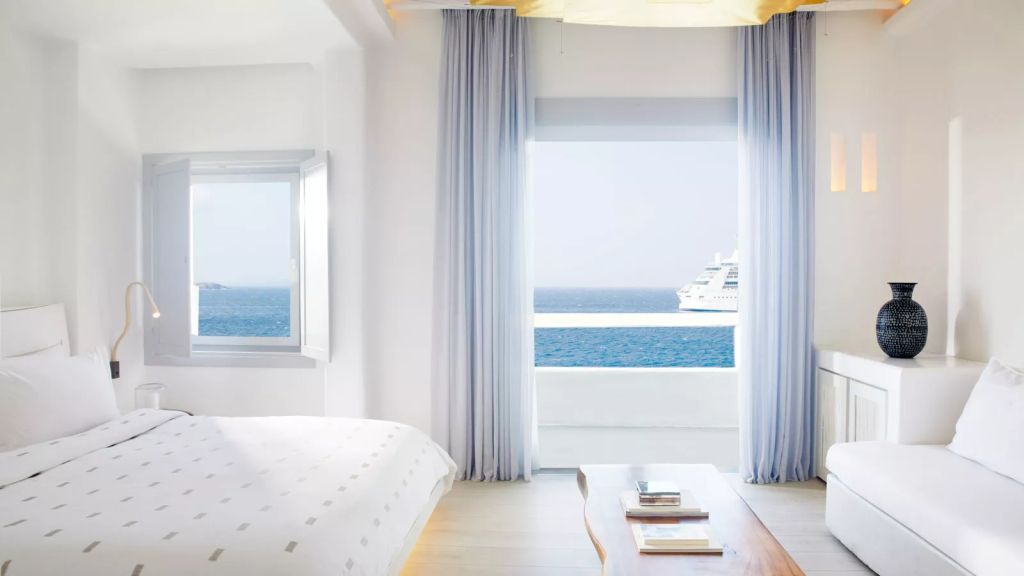 Zimmer mit offener Fensterfront und Blick auf das Meer und Kreuzfahrtschiff