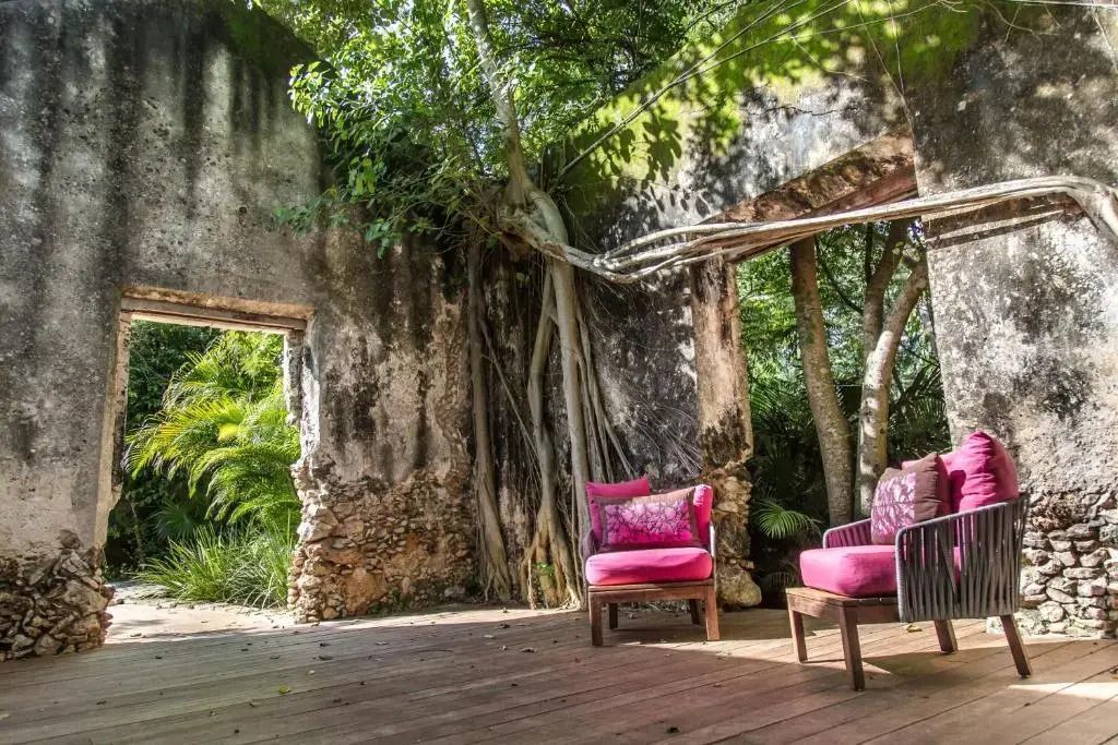 Tropische Terrasse mit antiker Steinwand und zwei pinkfarbenen Sesseln