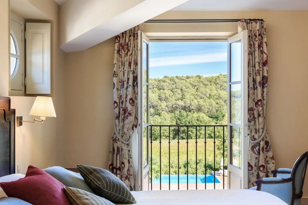 Zimmer mit offenem Fenster zeigt Blick auf grüne Landschaft und blauen Pool